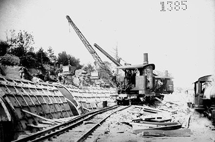 Using a hook rigged locomotive crane to pour concrete.