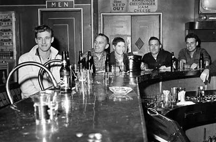 Patrons seated around a bar with a bottle of P.O.C. in the foreground