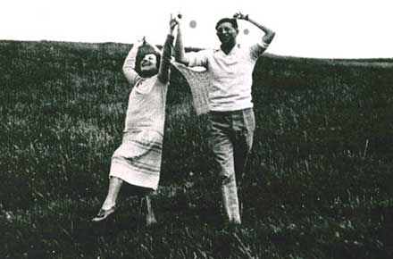 Authors Louis Bromfield and Edna Ferber hold hands and dance through a field of grass