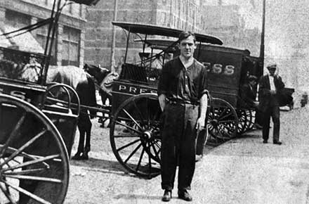 Man standing in front of Press's horse-drawn carriages.